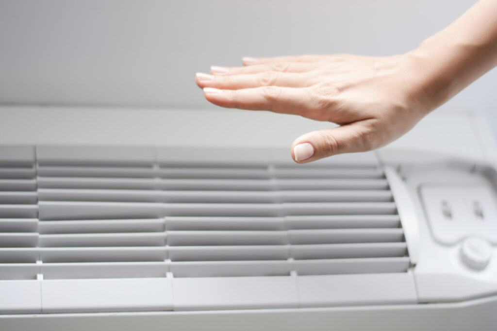Person's hand hovering over vents of ductless mini-split system, feeling the air coming through.