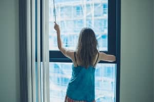 Woman closing vertical window blinds to block the sun.