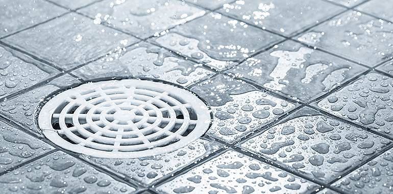 A flat white floor drain in a wet gray tile floor.