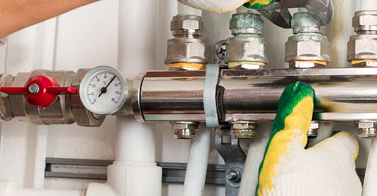 Close-up of technician's hands in gloves, servicing a backflow prevention device.