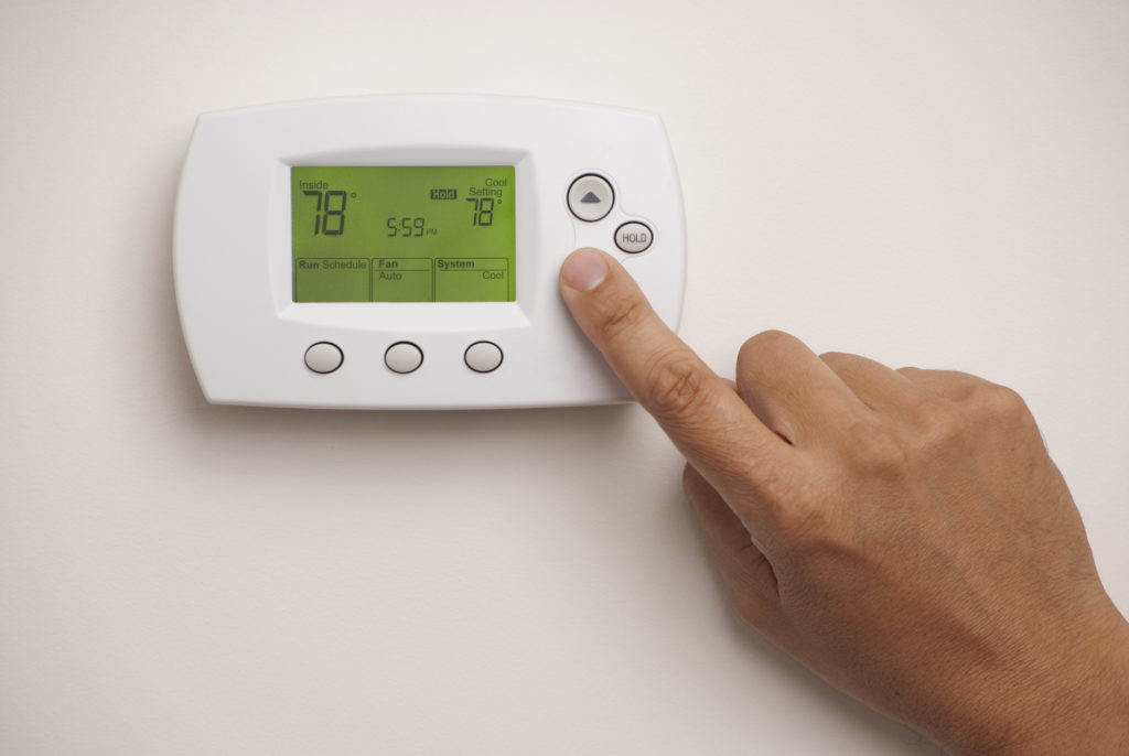 Digital thermostat with a male hand pressing a button, set to 78 degrees Fahrenheit.