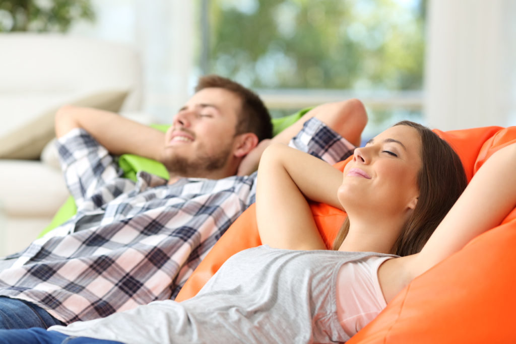 Couple or roommates relaxing at home, laying back and smiling with their eyes closed.